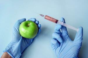 Green apple and syringe with GMO in hands on a blue background. photo