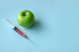Green apple and syringe with GMO on a blue background. photo
