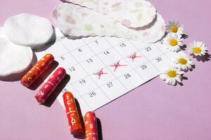 Menstrual pads and tampons on menstruation period calendar with chamomiles on pink background. photo