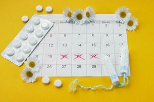 Menstrual pads and tampons on menstruation period calendar with chamomiles on yellow background. photo