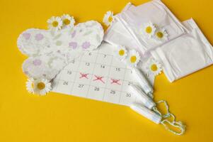 Menstrual pads and tampons on menstruation period calendar with chamomiles on yellow background. photo