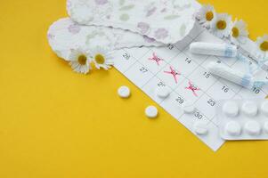 Menstrual pads and tampons on menstruation period calendar with chamomiles on yellow background. photo