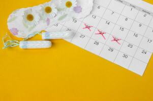 Menstrual pads with chamomiles on menstruation period calendar on yellow background. photo