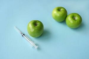 Green apple and syringe with GMO on a blue background. photo