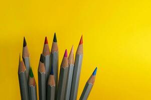 Many colorful pencils laying on yellow background. photo
