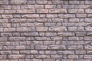 A modern stone fence in the form of an aged stone fence painted with light pink paint. photo