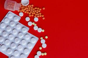 Assorted pharmaceutical medicine pills, tablets and capsules on red background photo