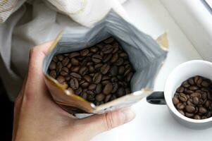 Hand holds an open package of coffee beans. photo