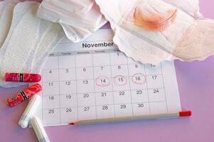 Menstrual pads and tampons on menstruation period calendar with on lilac background. photo