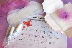 Menstrual pads and tampons on menstruation period calendar with on lilac background. photo