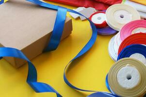 Gift box packaging on a yellow background. A lot of bright satin ribbons. photo