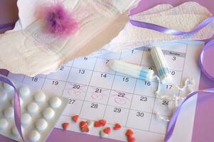 Menstrual pads and tampons on menstruation period calendar with on lilac background. photo