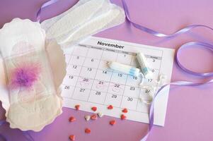 Menstrual pads and tampons on menstruation period calendar with on lilac background. photo