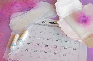 Menstrual pads and tampons on menstruation period calendar with on red background. photo