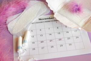 Menstrual pads and tampons on menstruation period calendar with on lilac background. photo