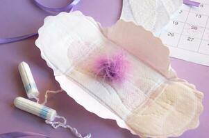 Menstrual pads and tampons on menstruation period calendar with on lilac background. photo