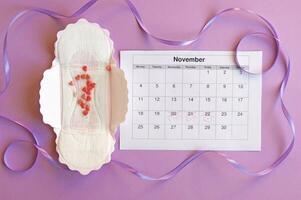 Menstrual pads and tampons on menstruation period calendar with on lilac background. photo