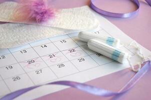 Menstrual tampons on menstruation period calendar with on lilac background. photo