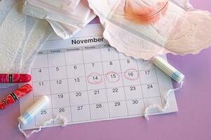 Menstrual pads and tampons on menstruation period calendar with on lilac background. photo