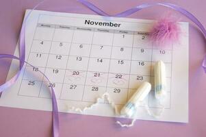 Menstrual pads and tampons on menstruation period calendar with on lilac background. photo