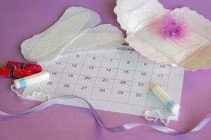 Menstrual pads and tampons on menstruation period calendar with on lilac background. photo