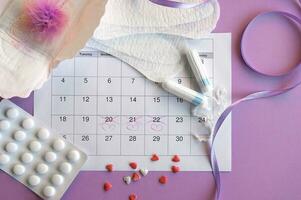 Menstrual pads and tampons on menstruation period calendar with on lilac background. photo