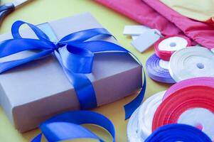 Gift box packaging on a yellow background. A lot of bright satin ribbons. photo