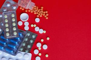 Assorted pharmaceutical medicine pills, tablets and capsules on red background photo