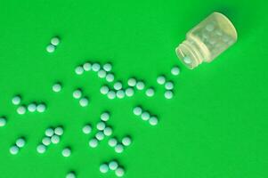 Inverted jar with orange pills on a green background photo