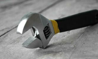 Adjustable wrench with yellow handle on the wood background photo