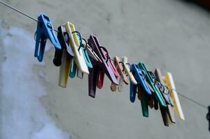 Multi-colored clothespins hang on a wire against the gray wall. photo