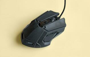 Matte modern black gaming mouse with buttons on a light yellow background. photo