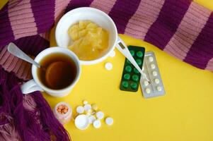 Cup of tea with lemon with pills and a thermometer on a yellow background. photo