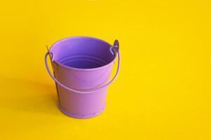 Miniature empty lilac bucket lies on a bright yellow background. photo