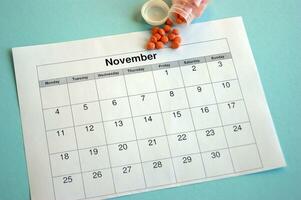 Inverted jar with orange pills and a calendar with marked dates on a blue background photo