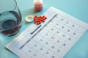 Inverted jar with orange pills and a calendar with marked dates on a blue background photo