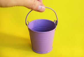 The miniature empty lilac bucket lies on a bright yellow backgroun photo