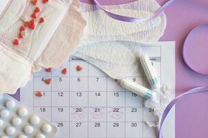 Menstrual pads and tampons on menstruation period calendar with on lilac background. photo