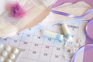 Menstrual pads and tampons on menstruation period calendar with on lilac background. photo