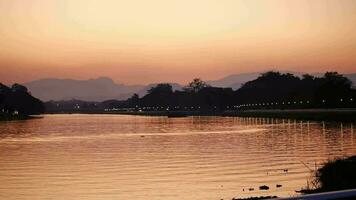 sole ambientazione al di sopra di il lago, come il sole imposta al di sopra di il in riva al lago, un' naturale paesaggio, bellissimo d'oro Alba al di sopra di il mare dietro a montagne nel sfondo video