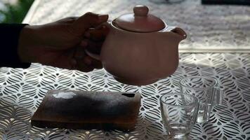 uma mão derramando chá a partir de vidro chaleira em de madeira servindo bandeja, mãos derramando chá a partir de bule de chá, cortada tiro do derramando chá dentro tradicional chinês chá porcelana video