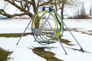 Children's playground in winter under snow. Swing, carousel and slide. Winter desolation photo