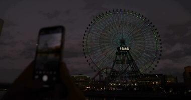 une crépuscule de tournant ferris roue tournage par téléphone intelligent dans yokohama video