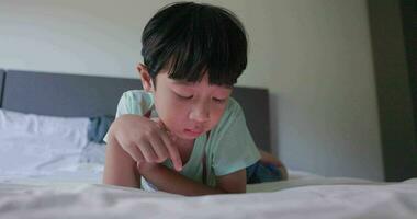 asiatique enfant avec noir cheveux avec une souriant visage mensonge dans lit en jouant avec une téléphone intelligent de le sien maison. prendre plaisir en utilisant le sien imagination. concept de enfants, apprentissage, la créativité, technologie, passe-temps. 4k video