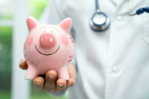 Doctor with Stethoscope holding piggy bank for saving money health care cost, medical financial. photo