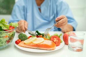 asiático mayor mujer paciente comiendo salmón filete desayuno con vegetal sano comida en hospital. foto