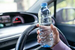 Asian woman driver holding bottle for drink water while driving a car. Plastic hot water bottle cause fire. photo