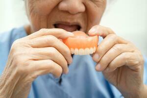 Asian elderly woman patient holding to use denture, healthy strong medical concept. photo