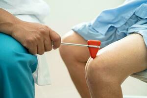 Asian doctor use hammer knock senior woman patient to check knee reflex, nerve and muscle in hospital. photo