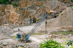 Mining in the granite quarry. Working mining machine - old crane and digger. Mining industry. photo